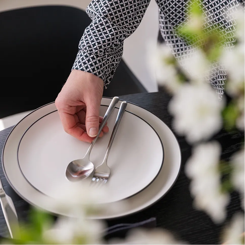 Une main pose les couverts Calgary sur une assiette blanche à bord noir