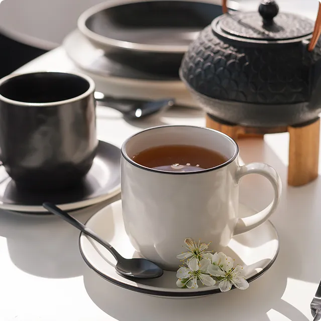 Tasse à thé blanche et noire sur une soucoupe près d'une théière noire