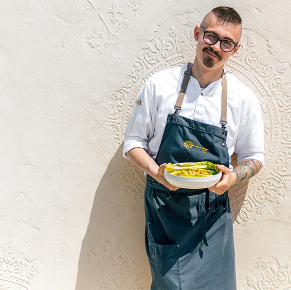 Un chef portant un tablier se tient près d’un mur et tient une assiette creuse contenant une salade César 