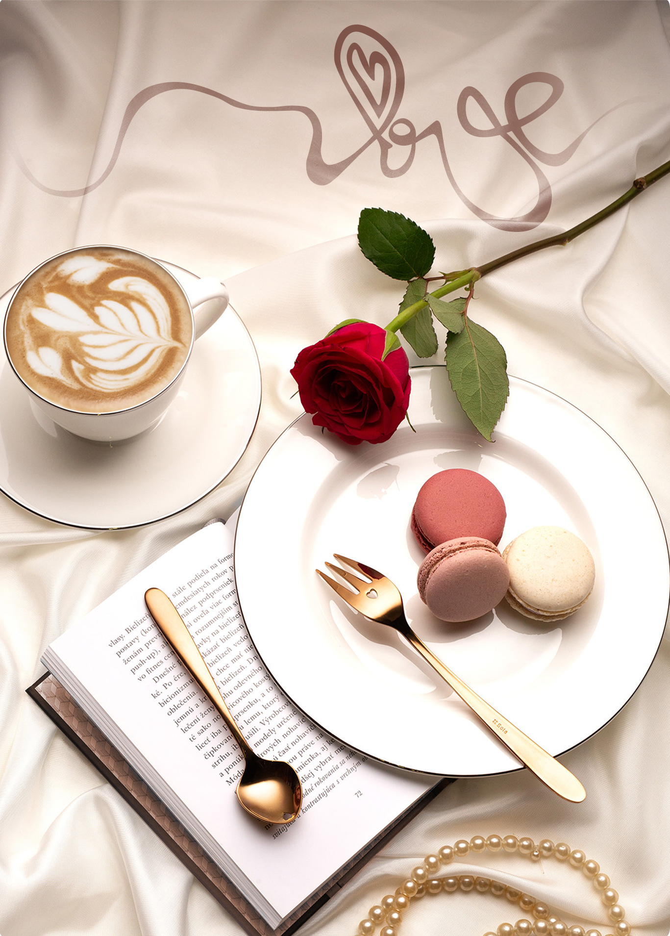 Une tasse de café, une rose rouge, des macarons, un livre et des couverts dorés sont posés sur un tissu satin blanc 