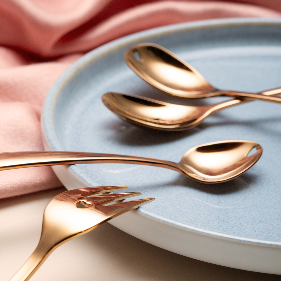 Des cuillères dorées et une fourchette sont posées sur une assiette bleu clair 