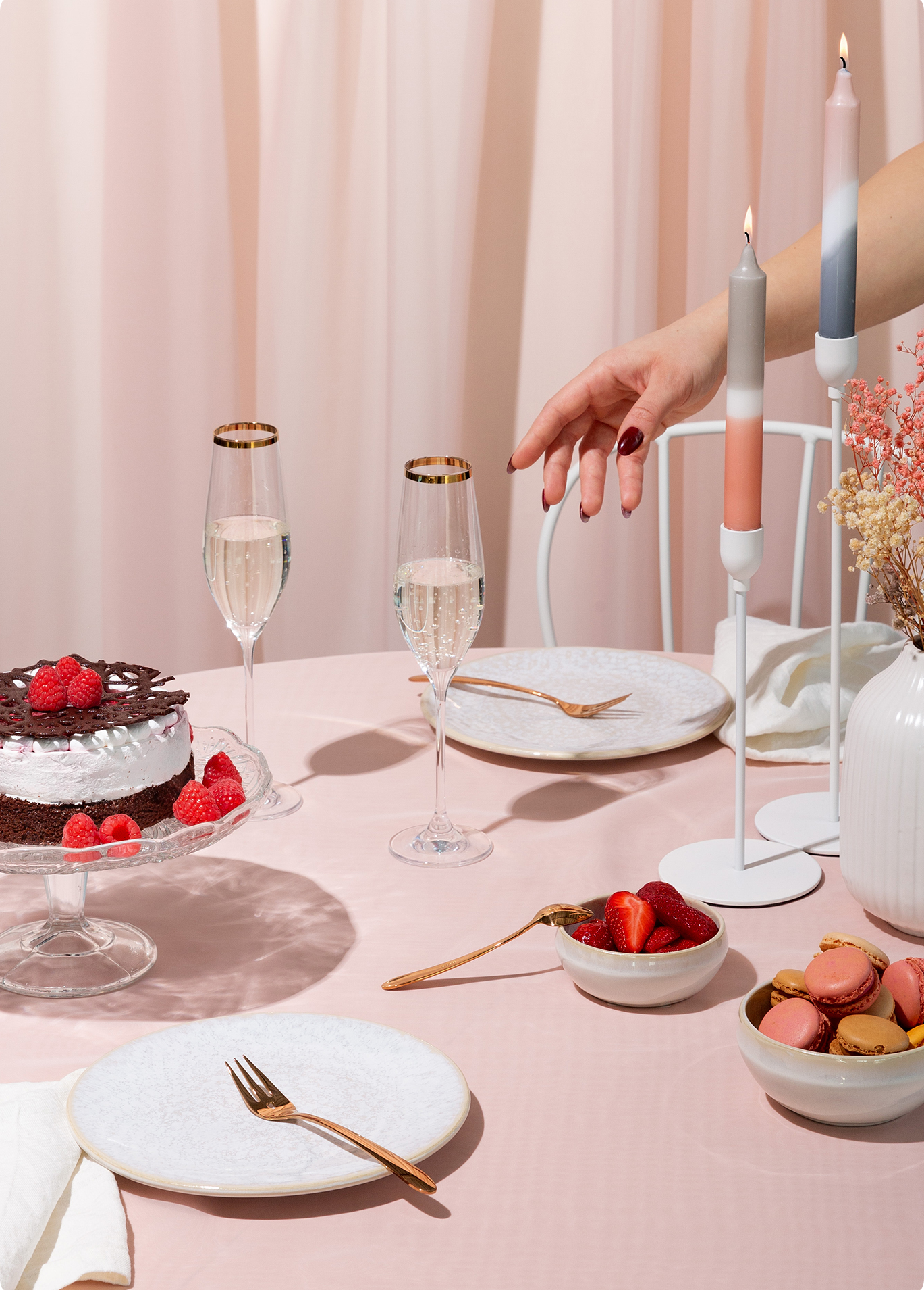 Une table dressée avec des desserts, des verres, des bougies et des couverts dorés sur une nappe rose 
