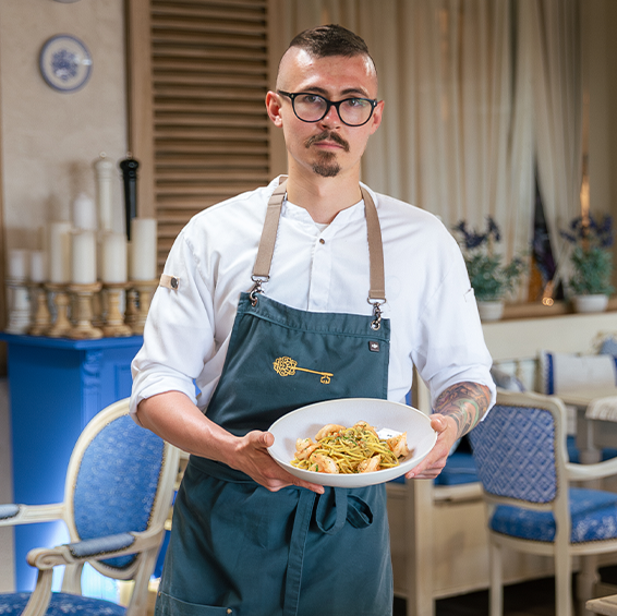 Un chef tient une assiette de spaghettis aux crevettes à l’intérieur d’un restaurant 