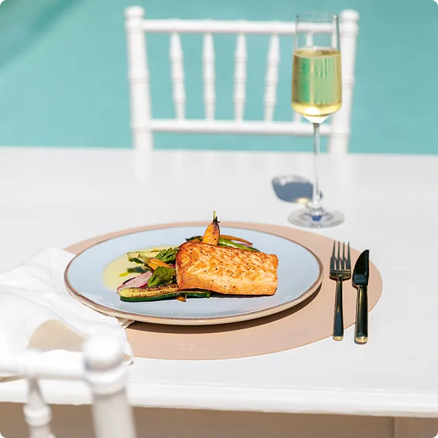 Saumon servi dans une assiette à côté d’une coupe de champagne et d’une piscine 